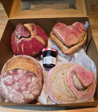 Load image into Gallery viewer, The Gift Box Valentines Day Mini Sourdoughs includes four artisan breads—two pink heart-shaped sourdoughs, a chocolate chip loaf, and another mini sourdough—paired with Bonne Maman strawberry preserve, presented on white parchment paper.
