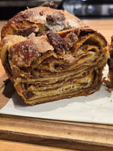 Load image into Gallery viewer, A loaf of sliced Pumpkin Babka with Candied Pecans swirled with candied pecans, topped with nuts and coarse sugar on a wooden board.

