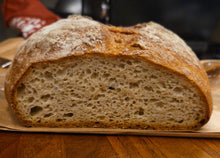 Load image into Gallery viewer, A close-up of half a Gluten free Artisan Boule showcases its golden-brown crust and airy, textured crumb as it rests on a wooden surface.

